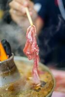 Man use chopsticks with thin pork for poached Thai soup with braised beef or pork, meatball, and vegetable in fire hot pot. photo