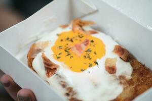 Hash brown topping with egg and bacon in paper box photo