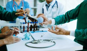 Medical team having a meeting with doctors in white lab coats and surgical scrubs seated at a table discussing a patients working online using computers in the medical industry photo