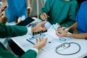 Medical team having a meeting with doctors in white lab coats and surgical scrubs seated at a table discussing a patients working online using computers in the medical industry photo