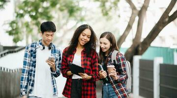 estudiantes son estudiando el instalaciones parque. joven personas son gasto hora juntos. leyendo libro, trabajando con ordenador portátil y tableta foto