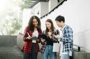 estudiantes son estudiando el instalaciones parque. joven personas son gasto hora juntos. leyendo libro, trabajando con computadora portátil, tableta y comunicado mientras foto