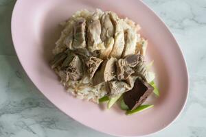 Steamed rice topped with boiled chicken and offal chicken on pink dish photo