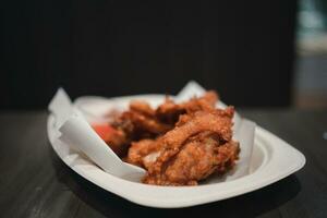 Fried chicken with sweet sauce in white paper plate on wooden table. photo