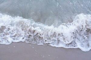 Soft wave with bubbles on sandy beach photo