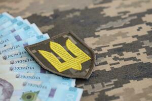 ucranio Ejército símbolo y manojo de hryvnia cuentas en militar uniforme. pagos a soldados de el ucranio ejército, sueldos a el militar foto