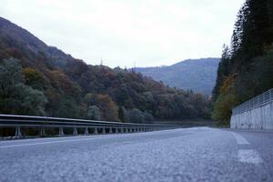 Road in autumn forest at sunset in Carpathian mountains, Ukraine. Beautiful mountain roadway with orange tress and high rocks. Landscape with empty highway through the woods in fall photo