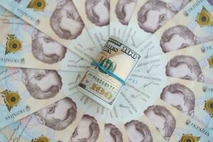 Bunch of hundred US dollar bills lies on many banknotes of ukrainian hryvnias. Economical default, crisis and devaluation of ukrainian national currency photo