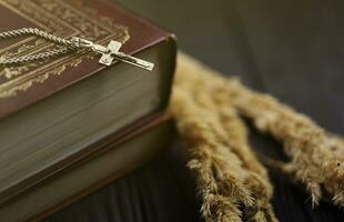 collar de plata con cruz crucifijo en el libro de la santa biblia cristiana sobre una mesa de madera negra. pidiendo bendiciones de dios con el poder de la santidad foto