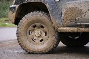 Wheel closeup in a countryside landscape with a mud road. Off-road 4x4 suv automobile with ditry body after drive in muddy road photo