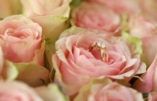 Gold diamond engagement ring in beautiful pink rose flower among big amount of roses in big bouquet close up photo