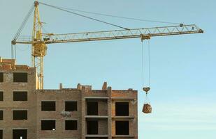 View of a large construction site with buildings under construction and multi-storey residential homes. Tower cranes in action on blue sky background. Housing renovation concept photo