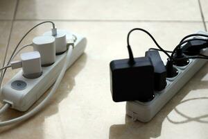 Overloaded power boards. Power strips with different electrical plugs on white floor photo