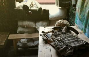 A military helmet of a Ukrainian soldier with a heavy bulletproof vest on wooden table in checkpoint dugout photo