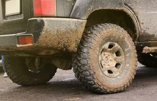 Wheel closeup in a countryside landscape with a mud road. Off-road 4x4 suv automobile with ditry body after drive in muddy road photo