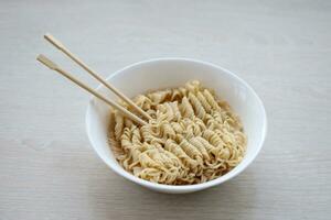 Bowl of instant cooking noodles with wooden chopsticks on white wooden table photo