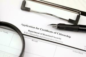 N-600 Application for Certificate of Citizenship blank form on A4 tablet lies on office table with pen and magnifying glass photo