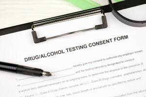 Drug and alcohol testing consent form on A4 tablet lies on office table with pen and magnifying glass photo