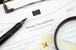 Schengen visa application on A4 tablet lies on office table with pen and magnifying glass photo