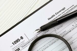 IRS Form 1095-B Health Coverage tax blank on A4 tablet lies on office table with pen and magnifying glass photo