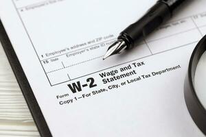IRS Form W-2 Wage and Tax Statement blank on A4 tablet lies on office table with pen and magnifying glass photo