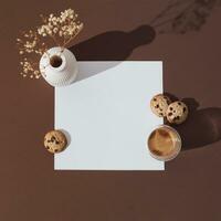 Creative trendy layout made with cup of coffee, chocolate cookies, white vase with dry flowers and paper card note copy space on espresso brown background. Minimal concept. Flat lay. photo