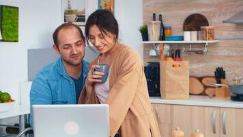 Happy entrepreneur couple working on laptop in kitchen during morning. Husband and wife cooking recipe food. Happy healthy together lifestyle. Family searching for online meal. Health fresh salad photo