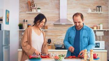 Pareja el cortar Tomates en de madera corte tablero para sano ensalada en cocina. Cocinando preparando sano orgánico comida contento juntos estilo de vida. alegre comida en familia con vegetales foto