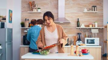 Husband kissing wife cheek while she is chopping bell pepper on cutting board in kitchen. Cooking preparing healthy organic food happy together lifestyle. Cheerful meal in family with vegetables photo