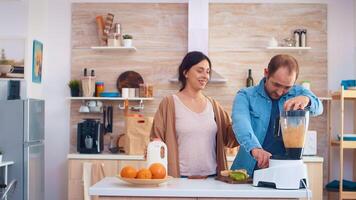 Man mixing fruits for smoothie using blender in kitchen. Cheerful young couple. Cheerful family making together organic healthy fresh nutritious tasty juice for breakfast from fresh fruits while on a diet. photo