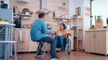 Unhappy disabled wife in wheelchair because of disagreement with husband in kitchen. Woman with paralysis handicap disability handicapped difficulties getting help for mobility from love and relationship photo