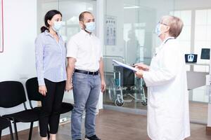 Unfavorable news from doctor to young couple in hospital waiting area during corona virus outbreak. Husband and wife wearing face mask against infection with covid 19. photo