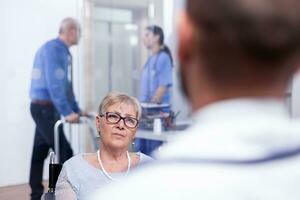 Handicapped woman in wheelchair at doctor appointment. Recovery treatment, help for disabled people. Elderly assistance. Old man with walking frame on hospital corridor. photo