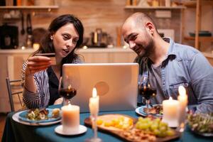 marido y esposa haciendo en línea pago durante romántico cena. adultos sentado a el mesa, buscando, hojeada, surf, utilizando tecnología tarjeta pago, Internet. foto