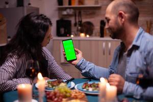 Couple looking at phone with green mock up having romantic dinner. Happy holding phone green screen template chroma key isolated smartphone display using technology internet. photo