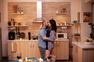 Young couple dancing in kitchen during romantic dinner. Happy in love couple dining together at home, enjoying the meal, smiling, having fun, celebrating their anniversary. photo