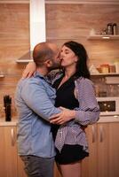 Husband kissing wife while dancing in kitchen. Happy in love couple dining together at home, enjoying the meal, smiling, having fun, celebrating their anniversary. photo