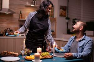 Pareja celebrando relación con romántico cena en comida habitación. mujer preparando festivo cena con sano alimento, Cocinando para su hombre romántico cena, hablando, sentado a mesa foto