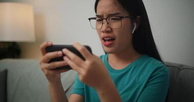 retrato de joven asiático mujer grave jugando un en línea juego frustrado con pérdida o fracaso sentado en sofá en vivo habitación a casa.jugador estilo de vida concepto. foto