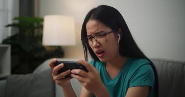 Portrait of Young Asian woman serious playing an online game frustrated with loss or failure sitting on sofa in living room at home.Gamer lifestyle concept. photo