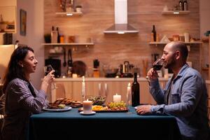 Pareja disfrutando un vaso de vino. relajarse contento personas cantarín, sentado a mesa en cocina, disfrutando el comida, celebrando aniversario en el comida habitación. foto