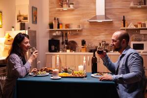 Young couple having romantic time during dinner. Happy couple talking, sitting at table in dining room, enjoying the meal, celebrating their anniversary at home having romantic time. photo