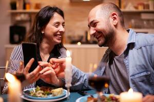 Cheerful couple laughing using smartphone during relationship anniversary. Adults sitting at the table in the kitchen browsing, searching, using smartphones, internet, celebrating . photo