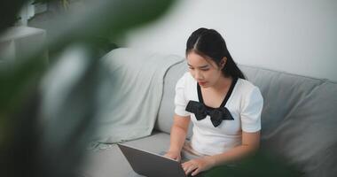 Portrait of Young asian woman relaxing at home sit on comfortable couch using laptop, chatting with friends in social network, do remote job, shopping online photo