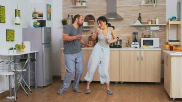 alegre Pareja bailando y canto durante desayuno en cocina vistiendo pijama. despreocupado esposa y marido riendo teniendo divertido gracioso disfrutando vida auténtico casado personas positivo contento relación foto