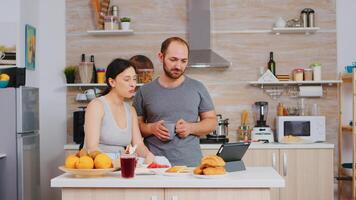 Couple waving during video call while eating delicious breakfast in kitchen. Videoconference in the morning, using online web internet technology, talking and communicating with relatives photo