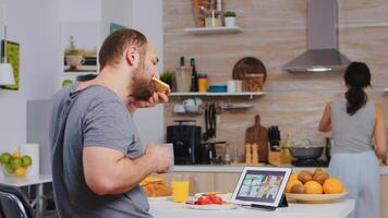 empresario en un vídeo conferencia mientras comiendo desayuno en cocina. persona de libre dedicación trabajando remoto, hablando en video conferencia vídeo llamada en línea web Internet reunión desde hogar, comunicación dispositivo foto