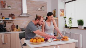 Young couple using laptop at the kitchen. Happy married husband and wife in pajamas using internet web online modern technology, smiling and happy in the morning. Reading news browsing internet photo