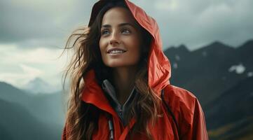 AI generated young smiling woman with a raincoat standing and looking at the mountains photo