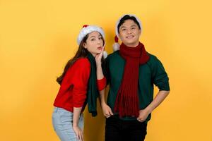 Asian man and woman wearing Santa hats on bright yellow background. Christmas and Happy New Year holiday concept. photo
